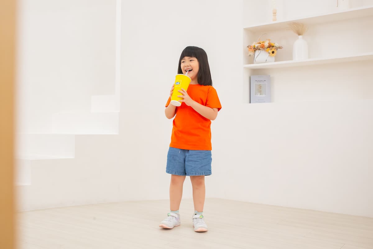 安新衣坊 KY T-K24 系列精梳棉兒童 T 恤亮橘色實穿展示，兒童模特兒開心拿著飲料呈現活動舒適度