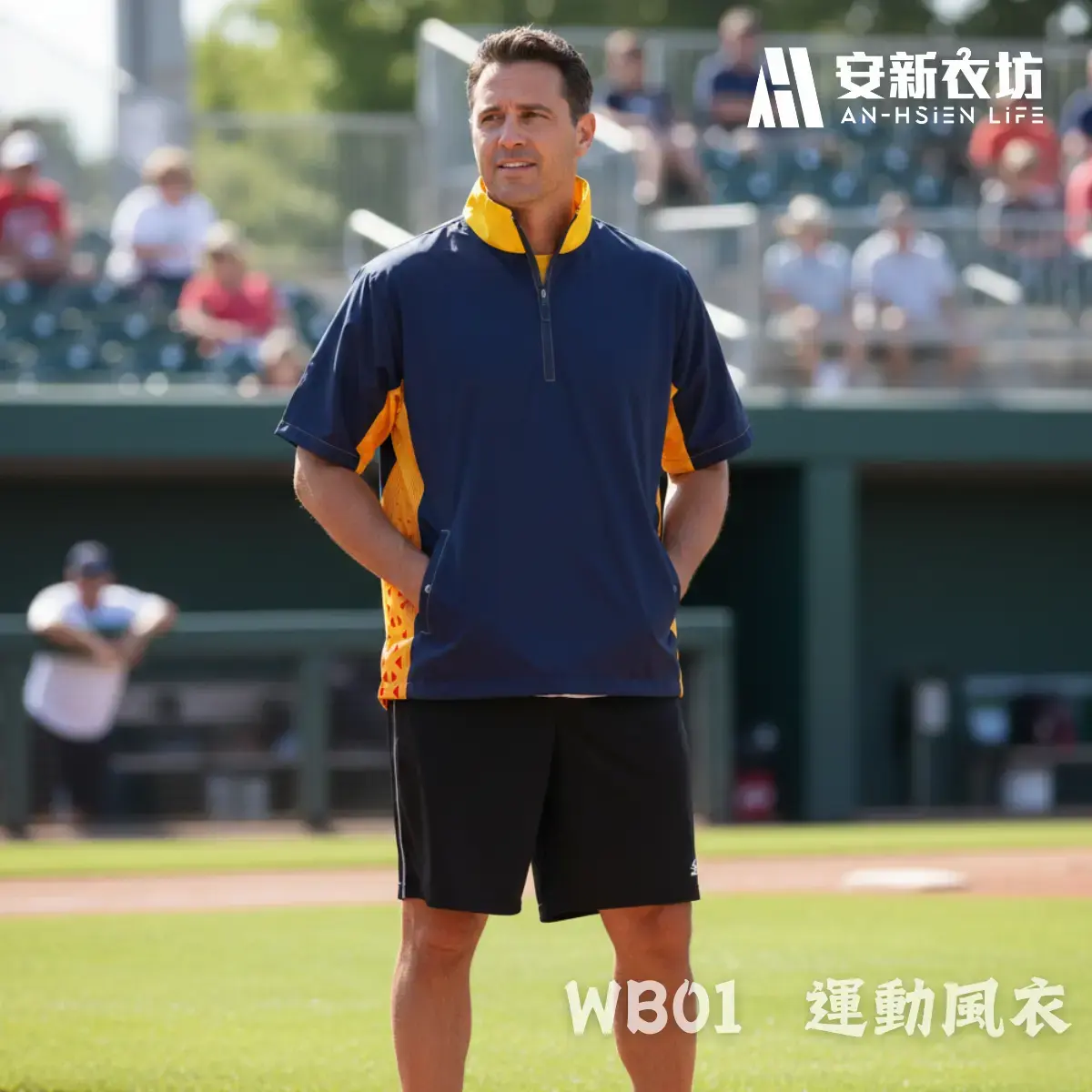 運動風衣WB01 安新衣坊WB01運動風衣專業男版實穿照。男模特兒於棒球場邊雙手插口袋,展示深藍與亮橘拼接的短袖半拉鍊防風外套。版型俐落沉穩,完美呈現棒壘球教練與球員的實戰熱身裝備。