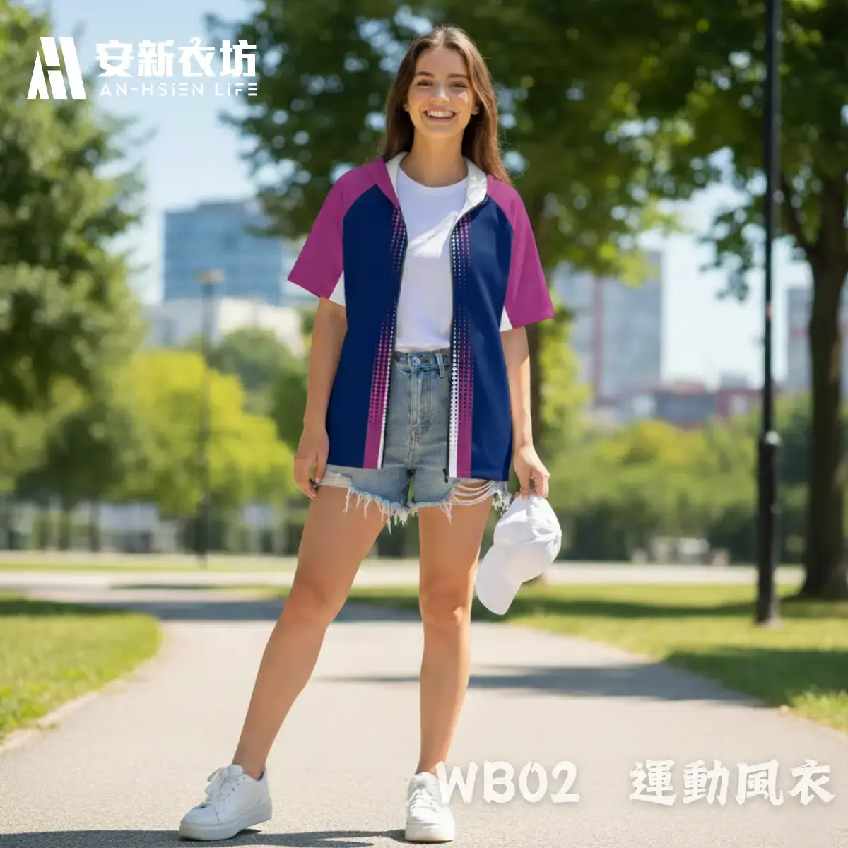 安新衣坊WB02運動風衣女版專業正面實穿照。女模特兒於都會公園展現陽光笑容，將深藍與紫紅拼接的短袖防風外套拉鍊全開，內搭白T恤與單寧短褲，完美詮釋胸前科技感漸層設計與日常運動休閒穿搭。