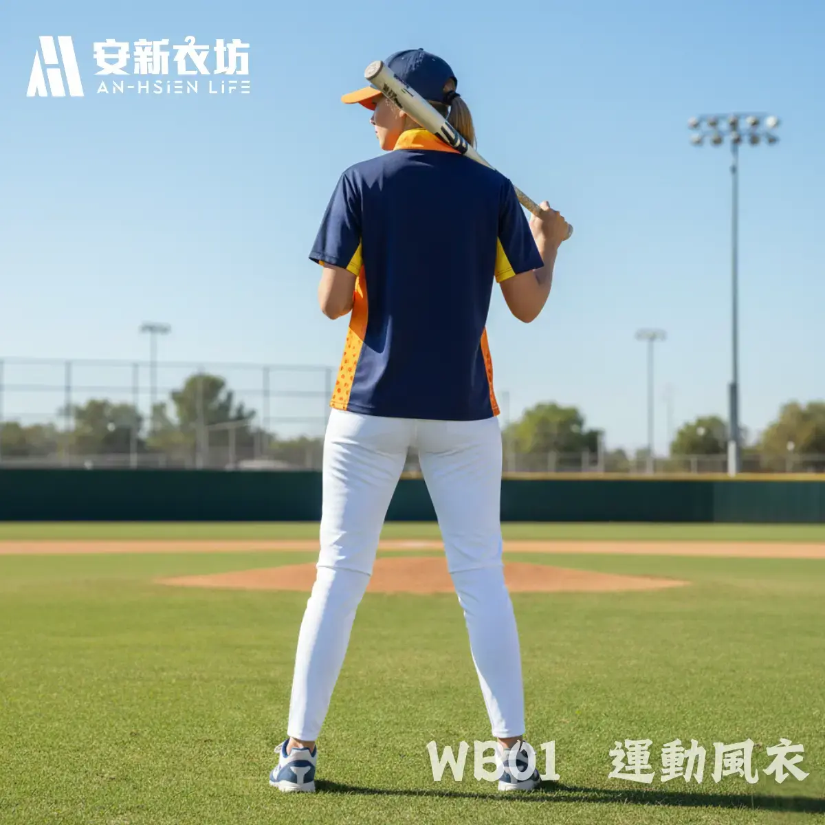 運動風衣WB01 安新衣坊WB01運動風衣專業實穿照背面視角。女模特兒於棒球場上背對鏡頭肩扛球棒,展示深藍與亮橘拼接短袖防風外套的背面修身剪裁,呈現大面積可客製化背號與姓名的平整布面。