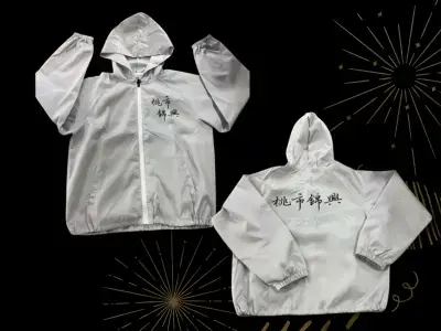 運動風衣 WB07 安新衣坊客製化長袖風衣實品照片,展示桃市錦興專屬防風外套。採用實用的連帽與全拉鍊設計(WB-L4版型),淺灰底色搭配充滿氣勢的黑色書法字體隊名,呈現經典俐落的校園團隊形象。