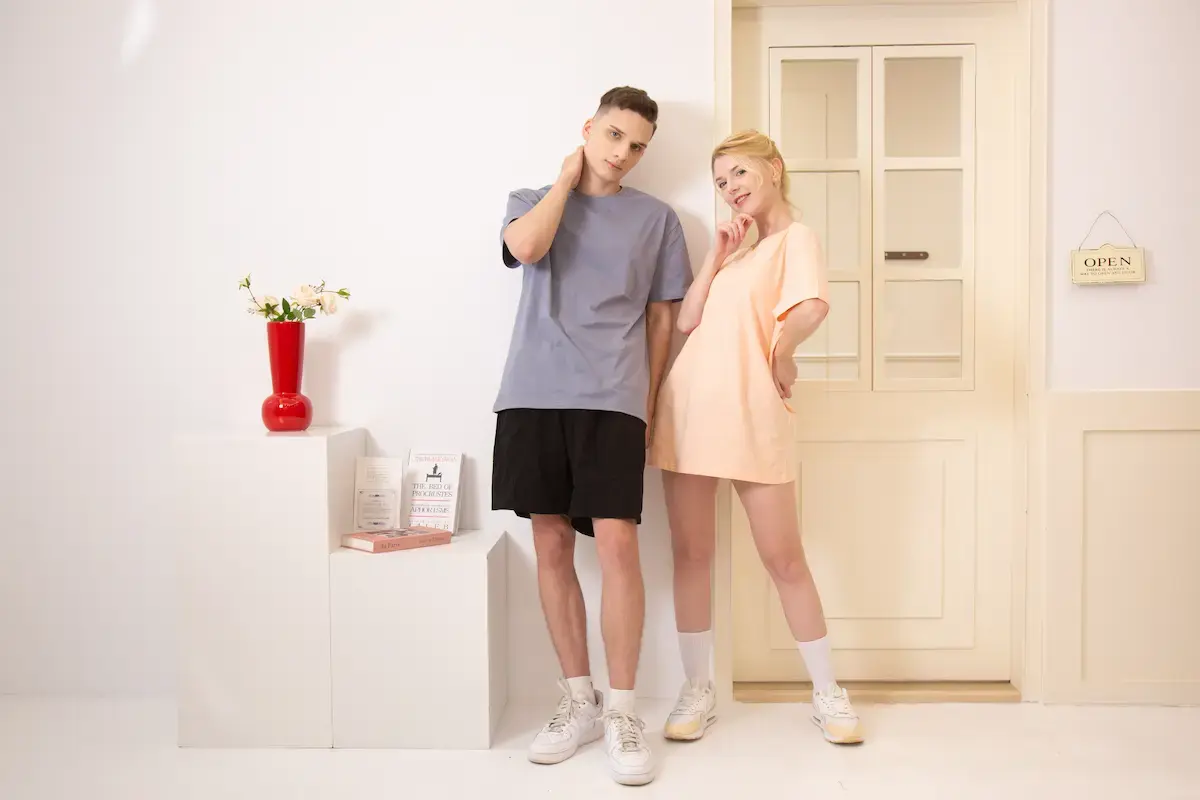 ARRIVE GUIDE AG18000頂級精梳棉T恤 一對男女模特兒靠在門邊展示 AG18000 精梳棉 T 恤,男生穿著雪青灰,女生穿著淺粉色長版 T 恤,展現清爽的春夏休閒穿搭感。