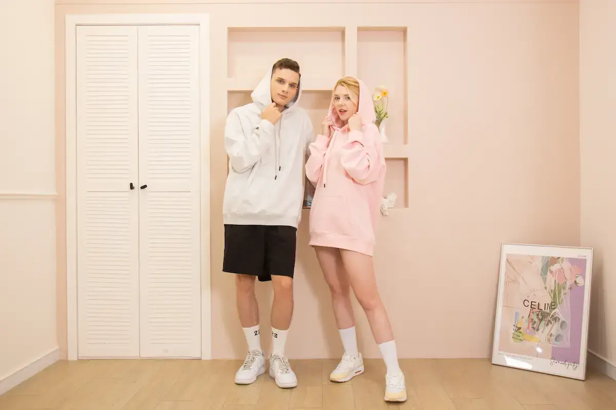 Arrive Guide AG2000 男女模特兒情境實穿照，展示雪花灰與珊瑚粉色重磅寬版落肩無刷毛連帽T。