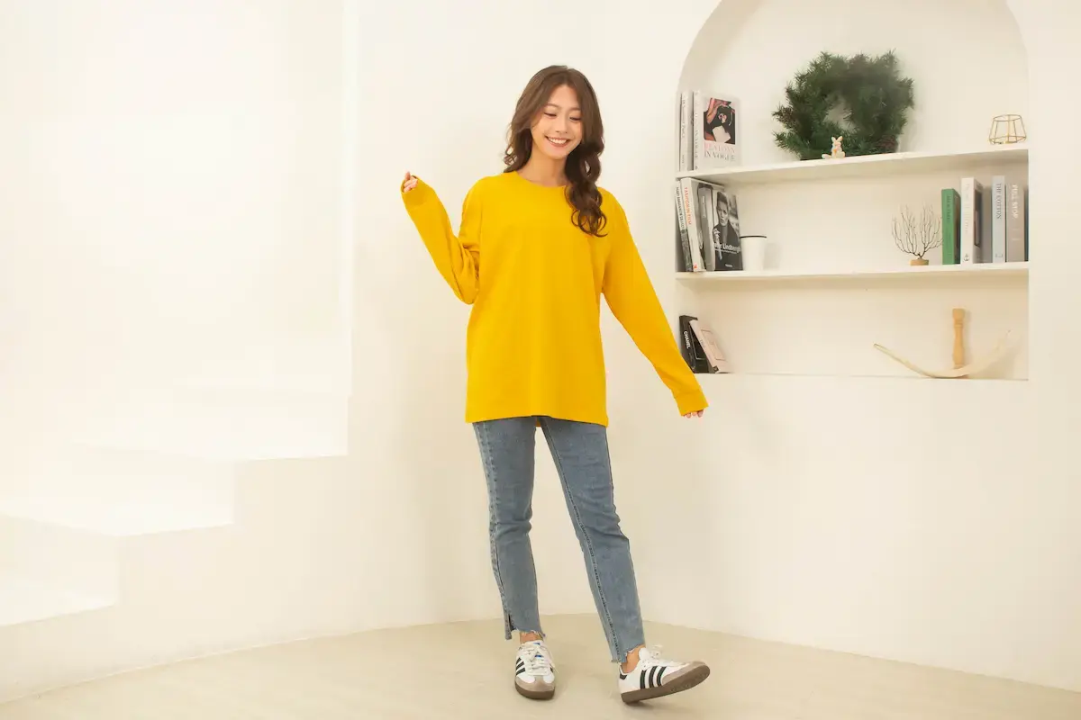 女模特兒穿著 Arrive Guide AG-L210 金黃色重磅長袖 T 恤，展現 210 克 40 支雙紗精梳棉的俐落質感與亞洲版型比例。